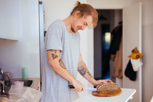 Skillful home baker slicing loaf on wooden surface with focus
