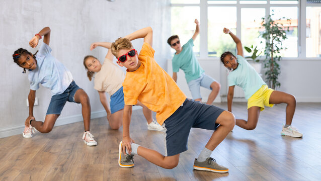 Smiling preteenage boy and girl in sunglasses dancer practicing active dance in modern studio