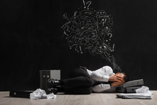 Businessman with folders lying near drawn thoughts on black wall. International Stress Awareness Week