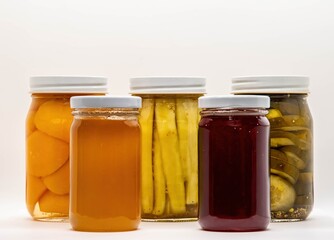 Jars filled with colorful homemade preserves sit on display. The collection includes peaches, pickles, and a sweet red fruit spread. These treats highlight seasonal bounty and canning skills.