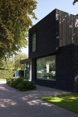 Modern architecture displayed in a striking black building surrounded by greenery and a well-kept pathway on a sunny day in a suburban neighborhood