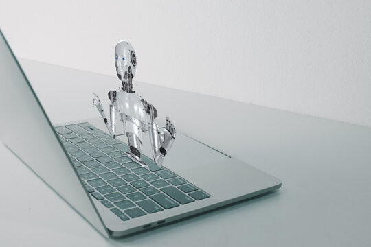Futuristic 3D humanoid robot emerging from laptop screen, representing artificial intelligence, chatbot assistant, virtual reality, and future technology concept on white office desk.