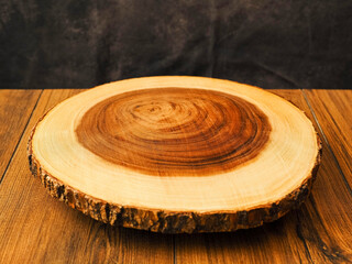 Premium round shape wooden cutting board on a wooden table, dark cloth background. Round shape kitchen tool with yellow and rich brown color tone. Woodcraft product with high quality finish.