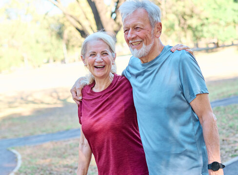 Smiling active senior couple jogging exercising and having fun and laughing together taking and walking a break in the park - Powered by Adobe