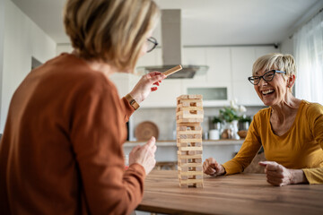 Senior women friends playing jenga game laughing at home