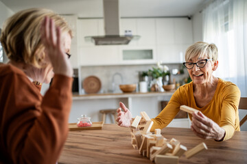 Senior women friends laughing while playing wooden block game together at home