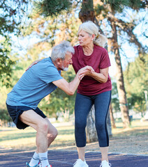 Fototapeta premium Active mid age senior mature couple jogging together, helping and supporting each other with a injury problem in the park