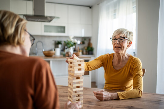 Senior women friends playing jenga board game at home