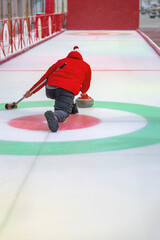 Obraz premium Outdoor curling player delivering stone towards circular target on frozen rink. Concept of winter sport precision, control and focused movement