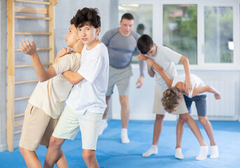 Obraz premium Determined teenagers sparring at self-defense training, trying to break free of back grab. Boys practicing basic techniques under guidance of experience instructor....