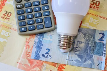 Conta de Luz (electricity bill in Portuguese) post-it reminder stuck on a light bulb, Brazilian Real banknotes and calculator. Electricity bill in Brazil concept.