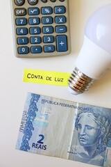 Conta de Luz (electricity bill in Portuguese) post-it reminder stuck on a light bulb, Brazilian Real banknotes and calculator. Electricity bill in Brazil concept.