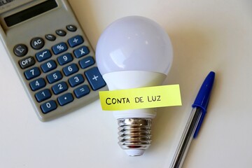 Conta de Luz (electricity bill in Portuguese) post-it reminder stuck on a light bulb and calculator. Electricity bill in Brazil concept.
