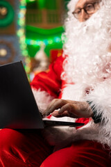 Naklejka premium Santa using laptop to spread Christmas spirit virtually by sending cheerful greetings. Father Christmas prepares personalized messages for families using notebook, sharing positivity and joy