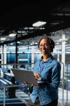 Portrait of black woman engineer solves maintenance tasks on laptop in high tech server hub, ensuring optimal performance and automation for software systems. Engineer reviewing diagnostics.