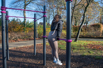 Young athletic woman performing triceps dips on parallel bars at an outdoor street workout park, staying active and focused on fitness during the fall season