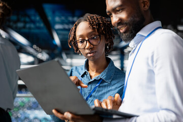 Supervisor and employee oversee performance outputs on server rigs for AI processing tasks. Server room specialists managing machine learning automation to ensure workflow, neural network.