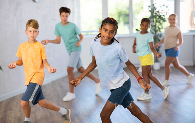Fototapeta premium Positive boy exercising in group of classmates during dance class at school