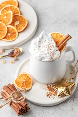 Hot cocoa drink with whipped cream, dried orange and spices in mug on white festive christmas table background