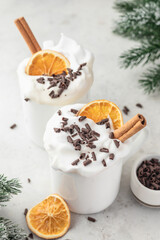 Hot chocolate drink with whipped cream, dried orange and spices in mug on white festive christmas table background