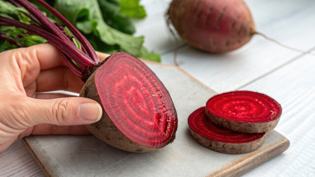 Freshly sliced beetroot held in hand with vibrant red interior on wooden board. Sliced beetroots showcase natural color and texture, perfect for healthy recipes or culinary blogs.
