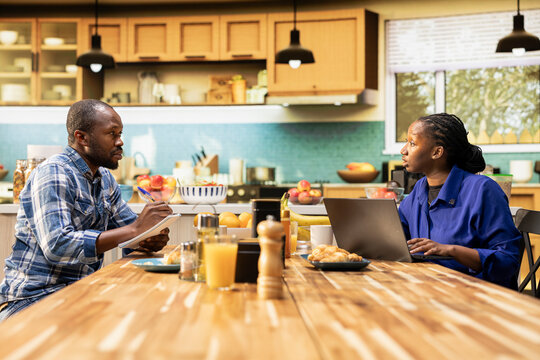 African American couple writing a grocery list together on a laptop. Man and woman planning shopping for essentials, groceries and household products online, healthy eating habits.