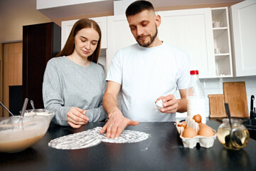 Couple enjoys cooking together in modern kitchen while preparing dough and cracking eggs during the weekend morning