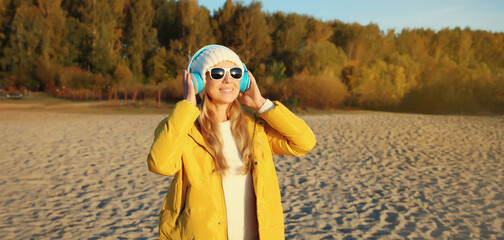 Happy inspired woman enjoying listening to music in headphones outdoors on autumn coast by the sea