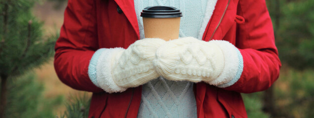 Close up female hand holding cup of hot coffee drink against Christmas tree in winter forest