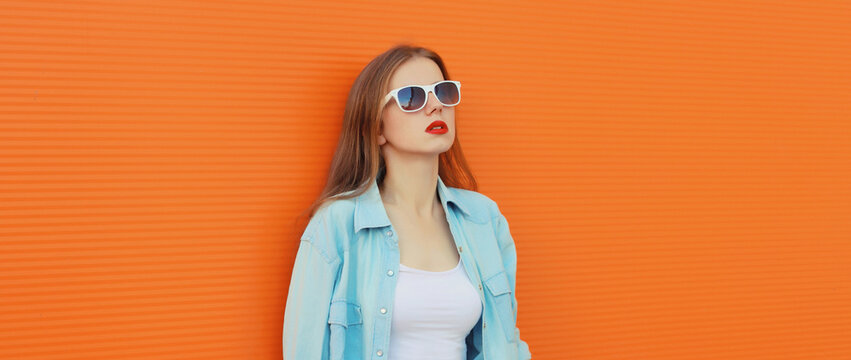 Portrait of modern stylish young woman in white glasses, casual clothing posing on orange background