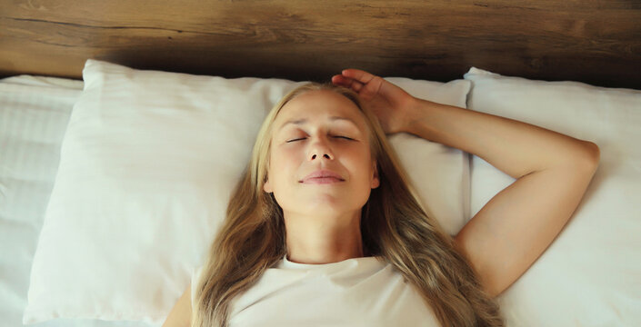 Woman sleeping lying in bed on white soft comfortable pillow in bedroom at home