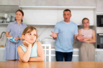 Obraz premium Sad preschooler girl sits at the table while parents and older sister scold