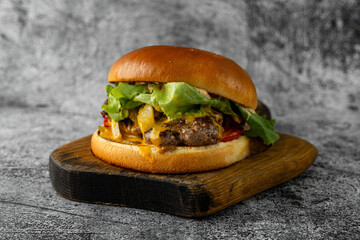 Savor the delicious layers of a juicy cheeseburger, perfectly grilled and adorned with crisp lettuce and ripe tomatoes, resting on a rustic wooden platter