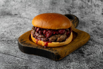 A delicious burger brimming with savory beef and a luscious berry sauce rests on a charming wooden board. This mouthwatering dish invites food lovers to savor its unique flavors