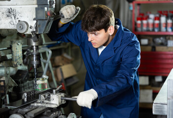 Young guy in uniform works with drill machine in metallurgical workshop