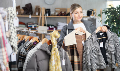 While shopping, woman browsing goods items and choose elect plaid jacket coat in store, buyer consider some items. Concept of seasonal wardrobe shopping. Client and holiday shopping.