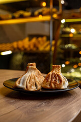 Two beautifully crafted dumplings rest on a sleek black plate, showcasing golden-brown edges. The warm atmosphere of the eatery enhances the inviting ambiance of the scene