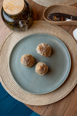 Three golden-brown spherical treats sit on a serene blue plate, surrounded by earthy textures and a cozy atmosphere, inviting a taste of comfort and warmth