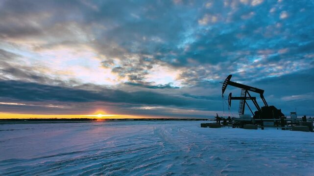 Winter sunset over a snowy Alberta oilfield with a pumpjack silhouette and a vehicle passing in the distance. Dramatic sky, industrial landscape and cold North American winter atmosphere.