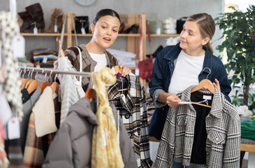 While shopping, women browsing goods items and choose elect something autumn outwear in store, buyer consider some items. Concept of seasonal wardrobe shopping. Client and holiday shopping.