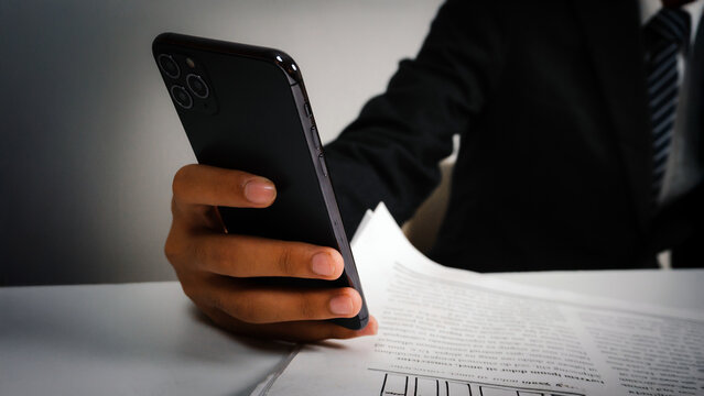 Businessman using smartphone at office desk for data transfer, online search, stock trading, and file downloading.