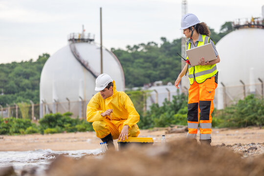 Environmental Scientists Sampling Water and Soil Near Industrial Chemical Storage Tanks, Chemical Engineer and Technician Taking Measurements and Inspecting Site Contamination