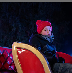 A portrait of a Boy in a red hat on a Christmas Carousel in an Evening Park
