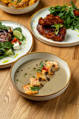 A delightful spread of gourmet food features a creamy soup garnished with grilled chicken pieces, alongside a fresh salad and grilled meat. Perfect for a cozy dining experience