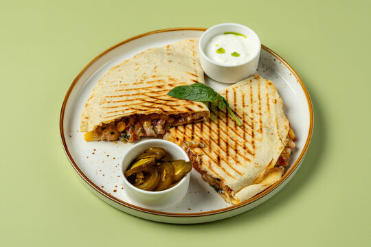 A plate showcases grilled quesadillas filled with delicious ingredients, accompanied by creamy sauce and tangy jalapenos, perfect for midday satisfaction