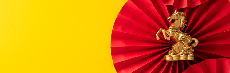 Golden horse figurine on a red paper fan against a bright yellow panoramic background.