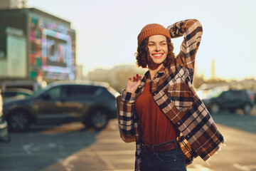Fototapeta premium Woman smile portrait in urban street at golden hour glow, candid lifestyle capture with authenticity and joyful expression, beanie and plaid coat, mindful living and emotional storytelling vibe.