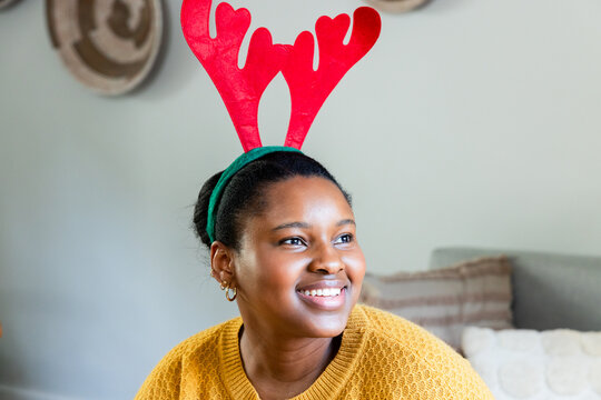 African American woman wearing red antler headband and sweater sitting on sofa at home with baskets