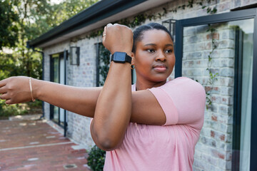 African American woman stretching arm on patio wearing smartwatch hoop earrings chain bracelet