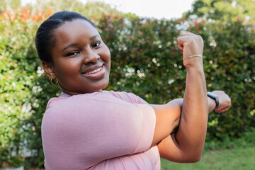 African American woman stretching bicep outdoors wearing pink T-shirt, smartwatch, hoop earrings